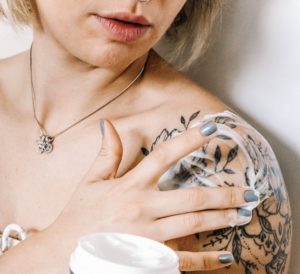 woman applying shea butter to tattoo - crushed vegan aftercare